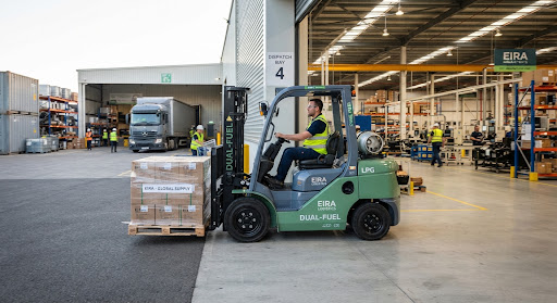 Heavy duty LPG dual-fuel industrial forklift operating seamlessly between an outdoor dispatch yard and an indoor manufacturing facility, clean green and slate colorway, high clarity industrial photograph